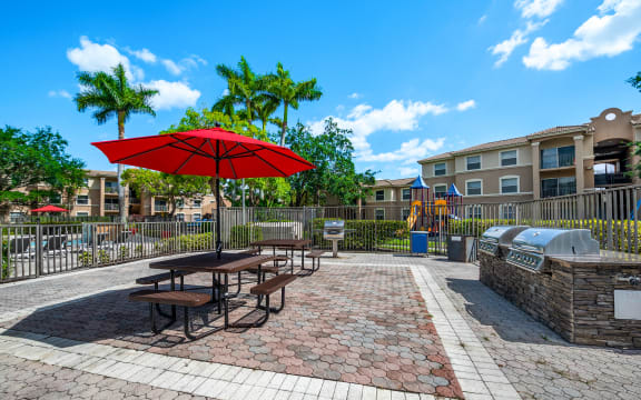 a picnic area with picnic tables and an umbrella in front of an apartment building at Pembroke Pines Landings, Pembroke Pines, 33025