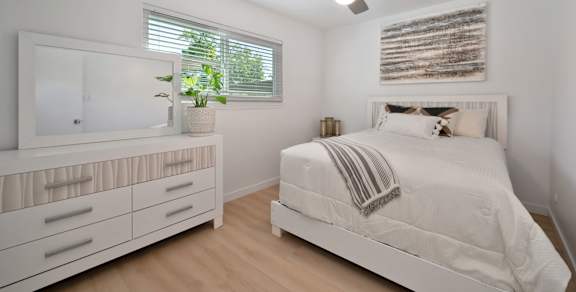 A white bedroom with a bed, dresser, and mirror.
