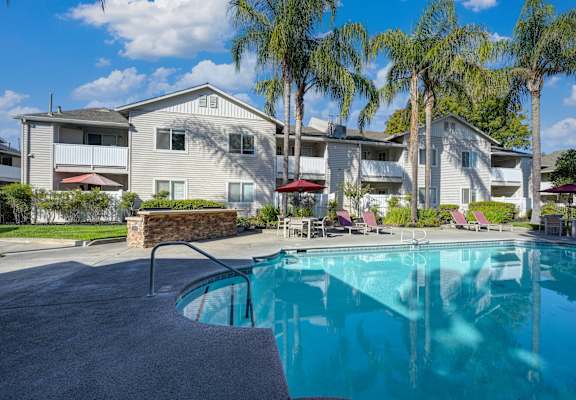 a swimming pool with palm trees in front of a house at The Legacy Apartments, California, 95843