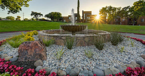 A garden with a fountain and flowers in the foreground with a building in the background at Fountains of Fair Oaks, Fair Oaks