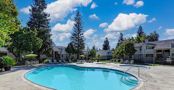 Monte Bello Swimming pool area with spa and apartment buildings in the distance.  Mature trees and blue skies in the background.