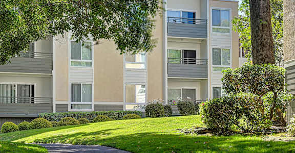A modern apartment building with a well-manicured lawn and trees in the foreground.