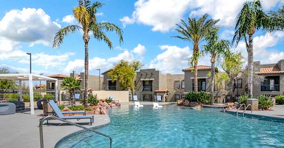 A pool surrounded by palm trees and a building in the background.