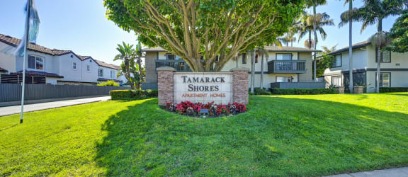 the entrance to tamarack shores apartments with a sign on the lawn and trees