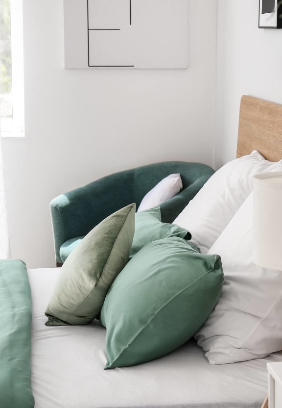 a bed with green and white pillows and a green chair