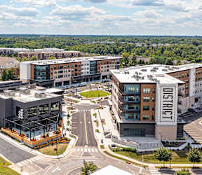 A city street with cars and buildings with a sign at The District at Deerfield Residences Apartments, Mason, OH, 45040