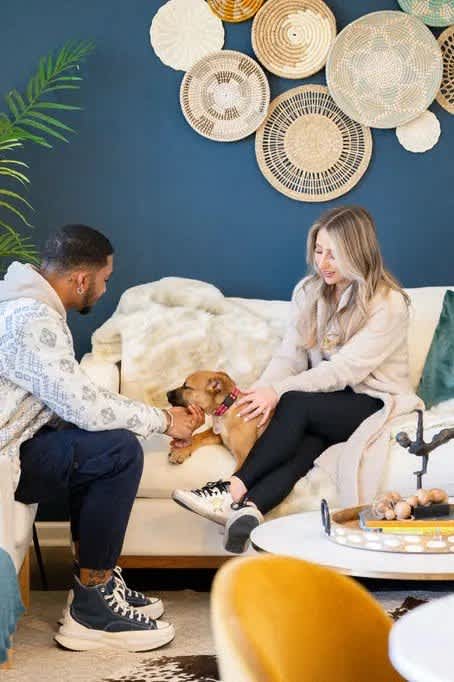 A man and woman sitting on a couch with a dog between them.