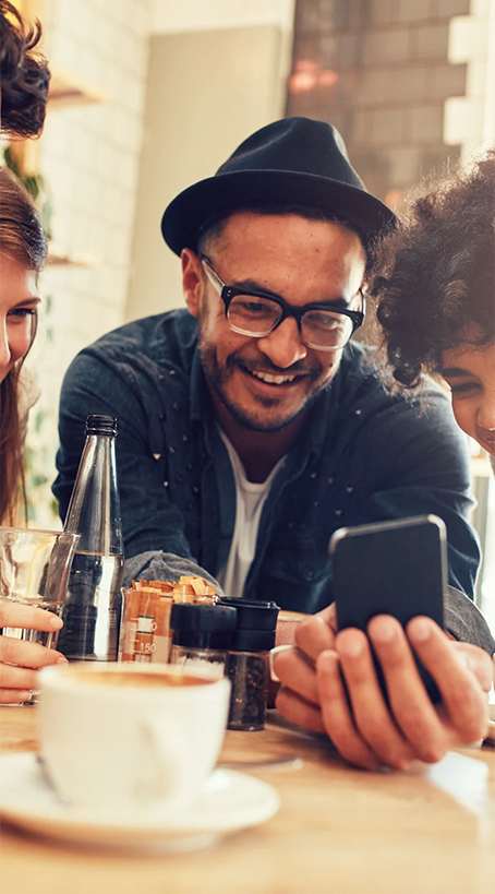 A man in a hat is using his phone while sitting at a table with a cup of coffee.