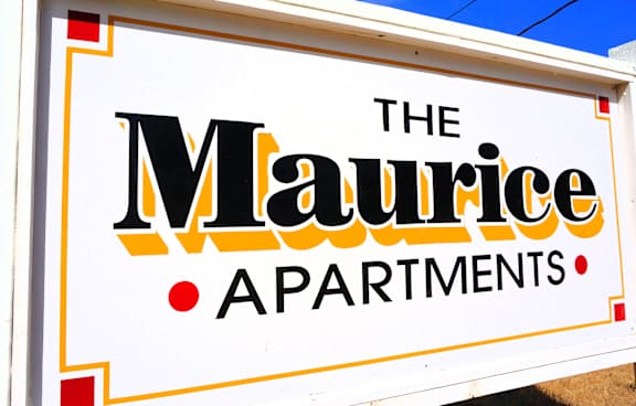 A sign for The Maurice Apartments is displayed on a sunny day.