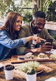 Three people are sitting at a table with food and drinks, looking at a phone.