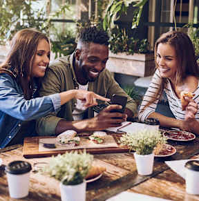 a group of people sitting around a table looking at a cell phone
