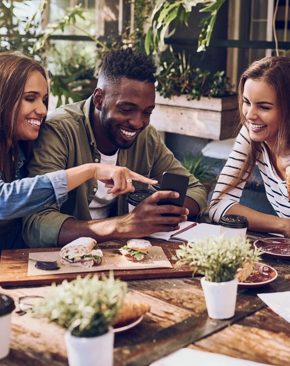 a group of people sitting around a table looking at a cell phone