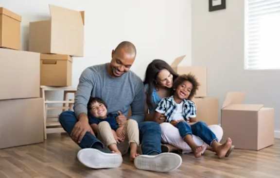A family of four sitting on the floor surrounded by moving boxes.
