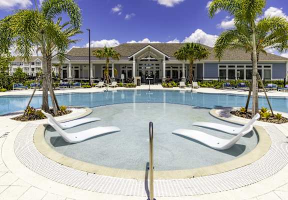a large swimming pool with white chairs and a building in the background
