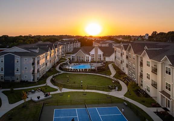 an aerial view of an apartment complex with a pool and tennis court at sunset at The Edison at Blue Springs, Blue Springs, MO, Missouri, 64014