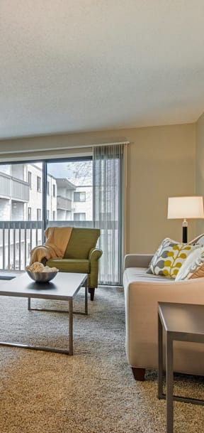 A living room with a couch, a coffee table, and a window with a view of a building. at Oakwood, Plymouth, MN, 55447