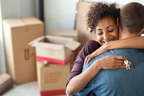 A couple hugging each other in a room with boxes in the background.