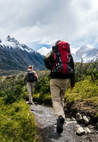 two people walking on a trail in the mountains
