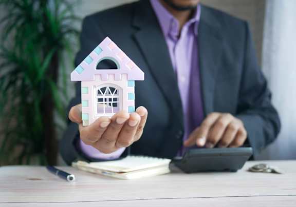 A man in a suit holding a small model house.