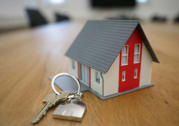 A small model house with a set of keys on a wooden table.