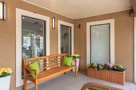 A wooden bench with green pillows sits in a room with a window and a flower box.