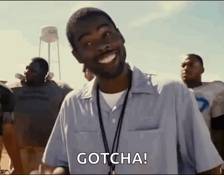 A man in a light blue shirt is standing in front of a group of people, with the word "GOTCHA!" in bold white letters at the top of the image.