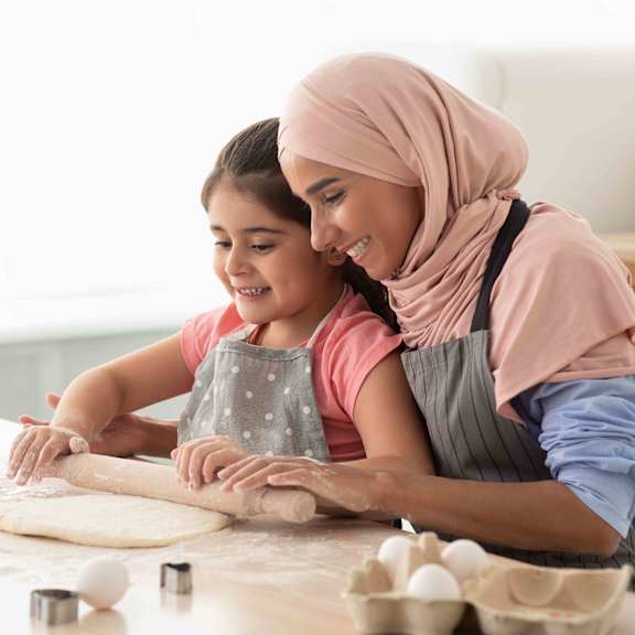 A woman and a young girl are rolling out dough on a kitchen counter.