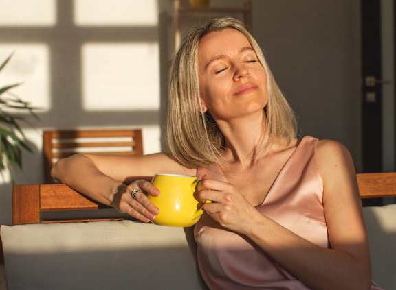 A woman in a pink dress is holding a yellow mug.