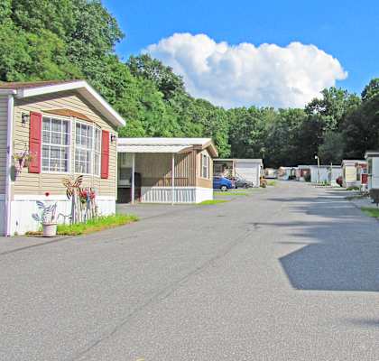A row of mobile homes with a tree-lined street in the background.