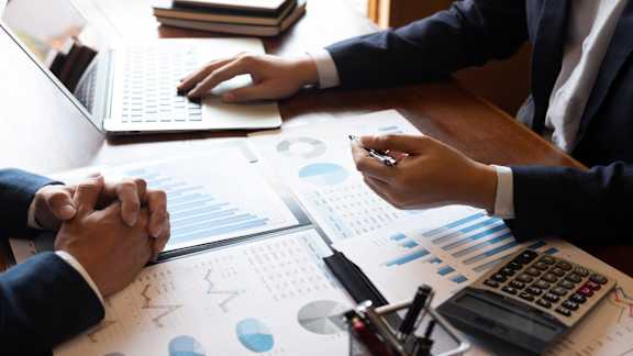 Two people in suits are analyzing financial charts and graphs on a table.