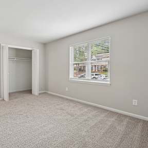A room with a white door, a window with blinds, and a carpeted floor.