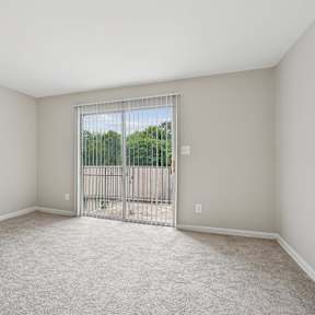 A room with a carpeted floor and a sliding glass door leading to a balcony.