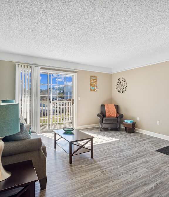 A living room with a grey couch, a green lamp, a wooden coffee table, and a white door.