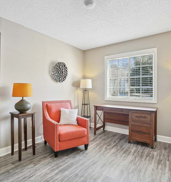 A room with a red chair, a lamp, and a desk.