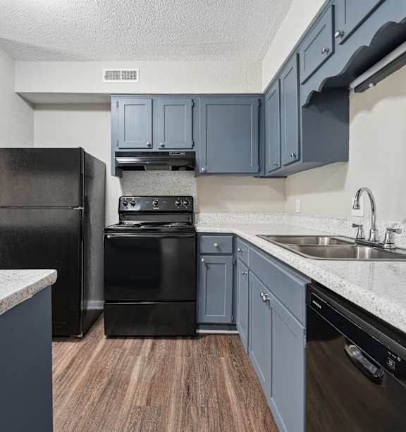 A kitchen with black appliances and wooden floors.