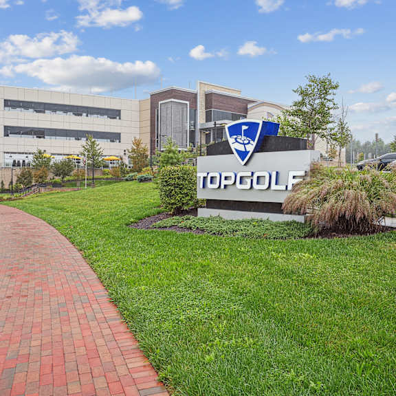A brick pathway leads to a Topgolf sign in front of a building.