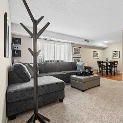 A living room with a grey couch, a tree-shaped object, and a shelf with various decorative items.