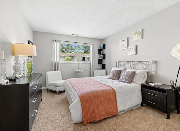 A bedroom with a bed, nightstand, and chair.