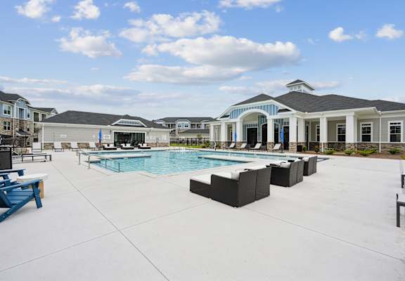 A large outdoor swimming pool area with sun loungers and a building in the background.
