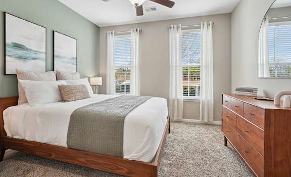 A bedroom with a bed, dresser, and window with curtains.