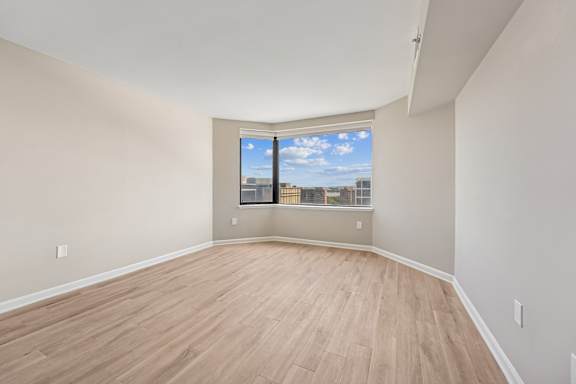 Empty room with wooden flooring and a window showing a cityscape.
