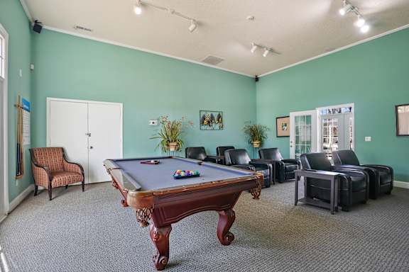 A room with a pool table and chairs.