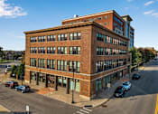 Thumbnail 1 of 14 - A street view of a red brick building with cars parked in front. at 100 South Apartments, Buffalo, 14202