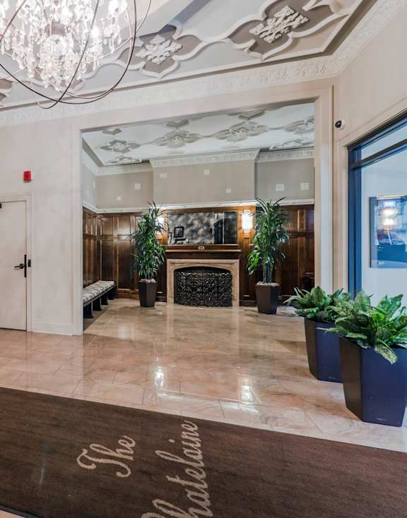 A foyer with a chandelier, a fireplace, and a rug that says "The Shalbina".