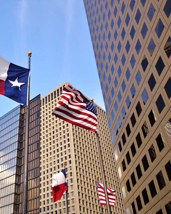 Flags of Texas and the United States flying in front of a building.
