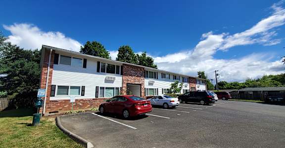 A red car is parked in a parking lot in front of a building.
