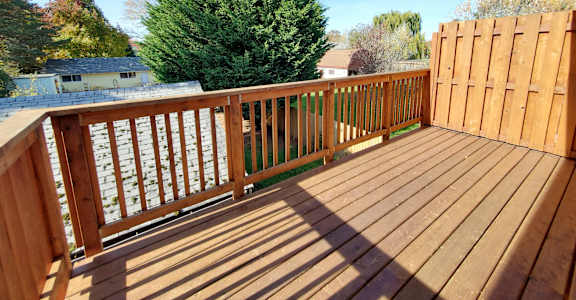 A wooden deck with a railing and a tree in the background.