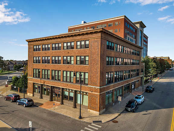 A street view of a red brick building with cars parked in front. at 100 South Apartments, Buffalo, 14202