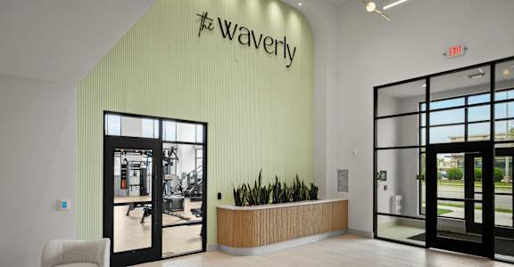 The lobby of The Waverly building with a white chair and a wooden table.
