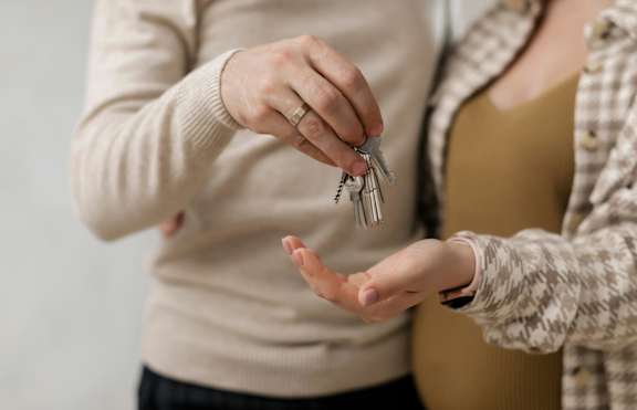 A person in a beige sweater is handing over a set of keys to another person.